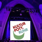 Logo des KulturPott.Ruhr vor der Kulisse der beleuchteten Bühne in der Heilig-Kreuz-Kirche