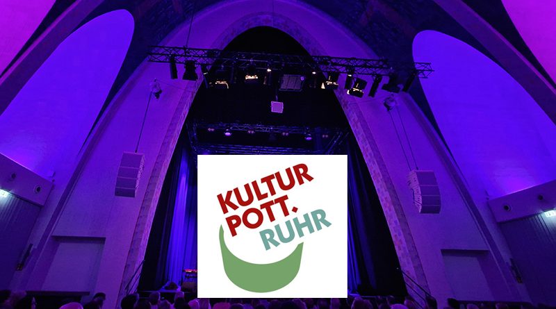 Logo des KulturPott.Ruhr vor der Kulisse der beleuchteten Bühne in der Heilig-Kreuz-Kirche