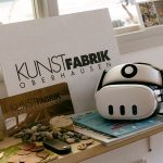 Eine Fensterbank auf der eine VR-Brille mit Büchern und einer Karte mit der Aufschrift Kunstfabrik zu sehen ist