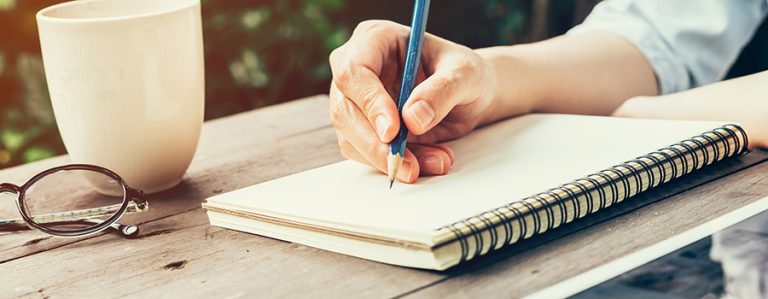 Female hand with pencil writing on notebook. Woman hand with pencil writing on notebook at coffee shop.